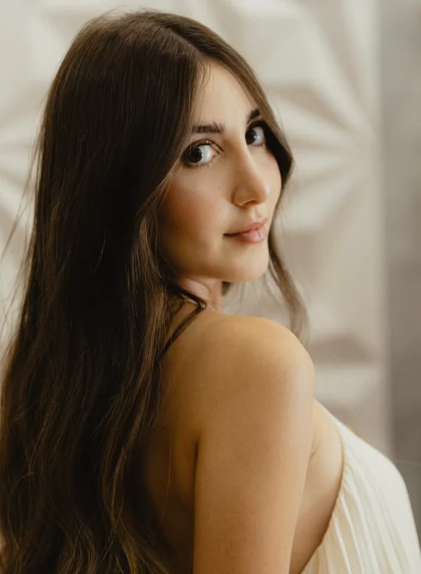 Isadora Mendes, de cabelos longos, olhando por cima do ombro, com vestido plissado creme